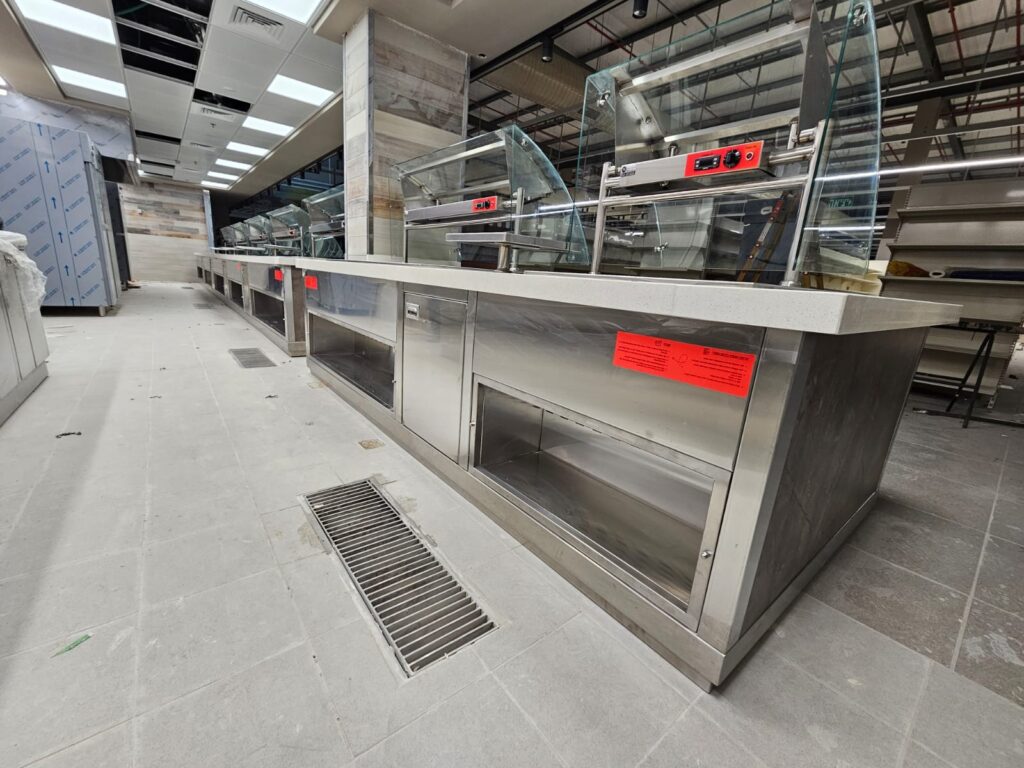תמונה של דלפק מזון מנירוסטה עם מכסי זכוכית, כנראה במסעדה או במזנון, במהלך בנייה או שיפוץ.